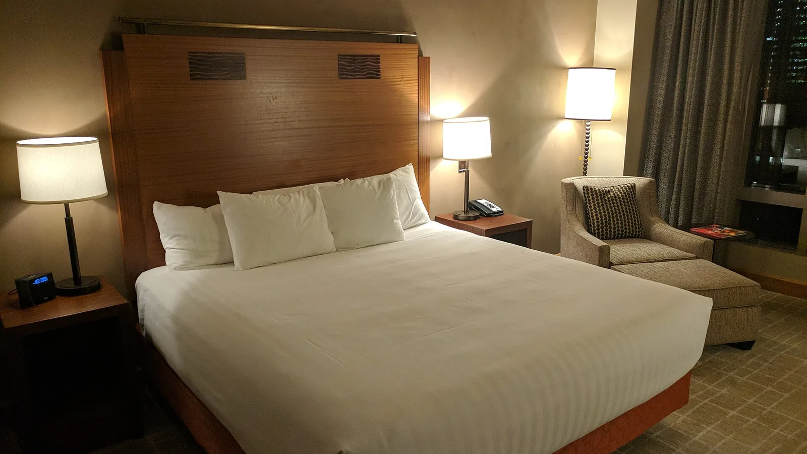 A made queen bed with white linen and pillows in a dimly lit room, bedside lamps on either side